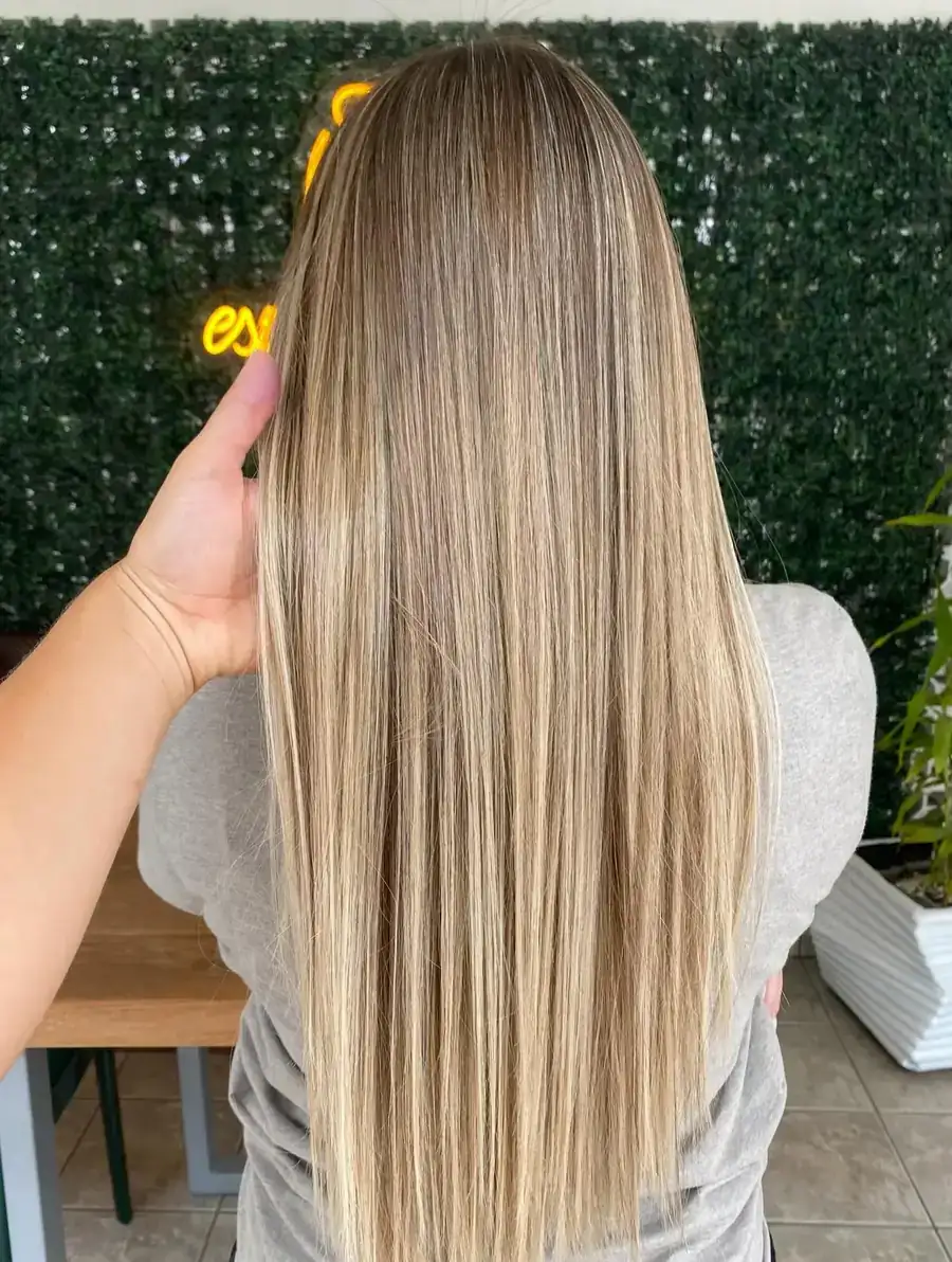 Cliente de costas diante do muro verde com o neon do Ollie, cabelo loiro com mechas, liso