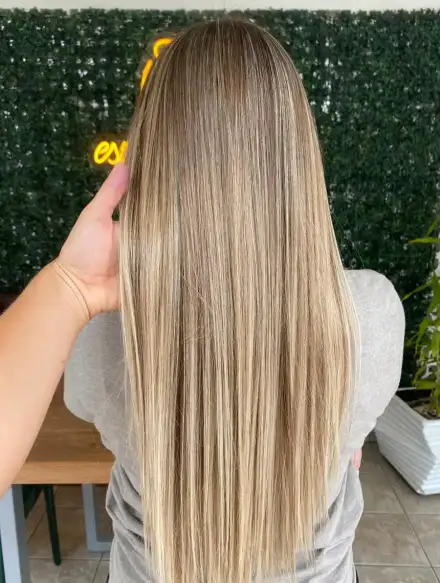 Cabelo loiro com mechas, liso, de costas diante do muro verde com o neon