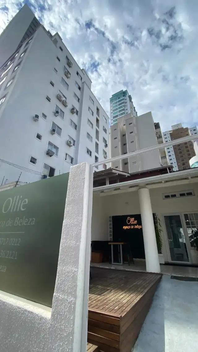 Fachada do Ollie: vidro com o letreiro, deque de madeira e prédios altos do Centro